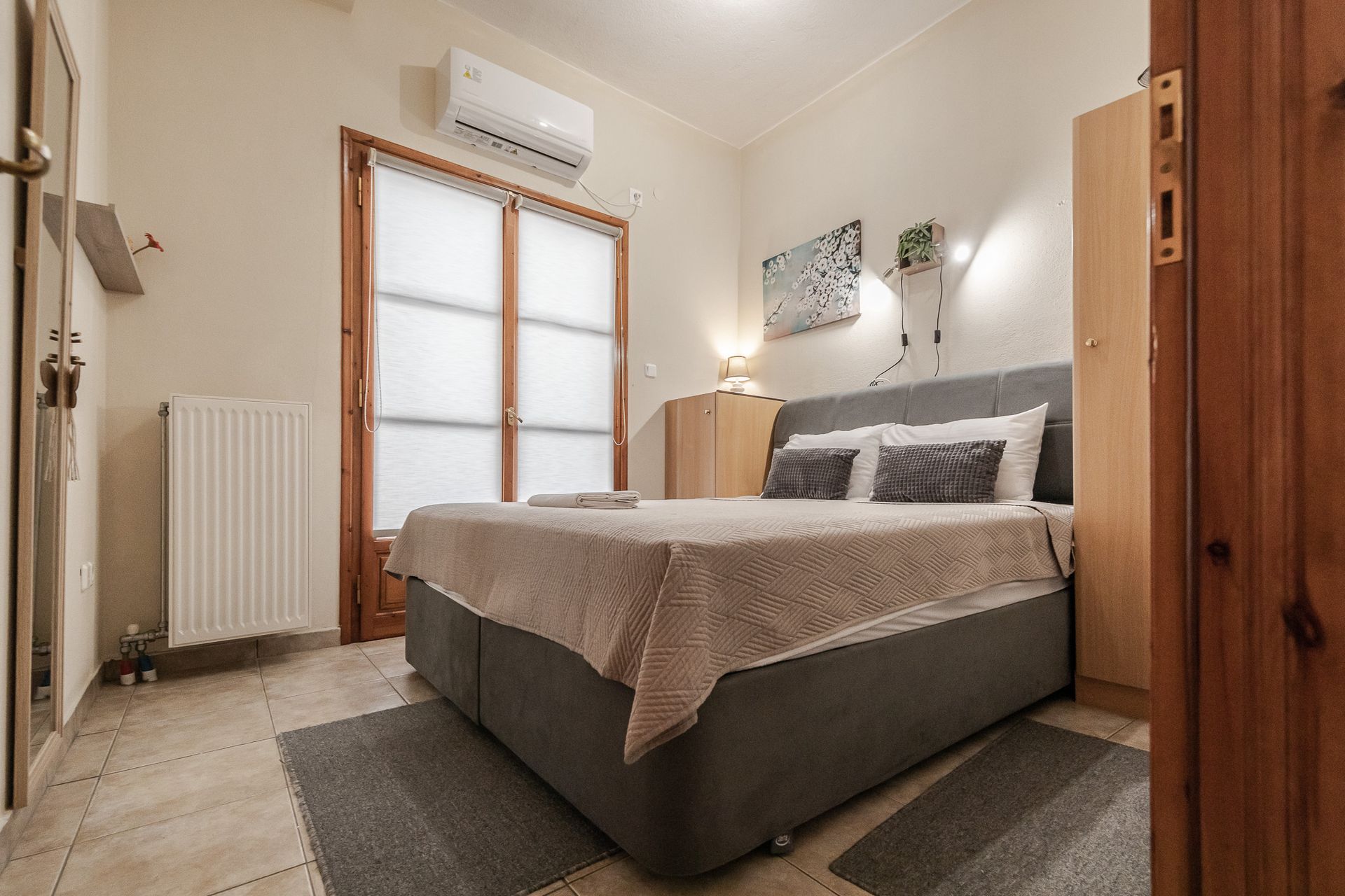 Small cozy bedroom with a bed, rug, radiator, and wardrobe under warm lighting