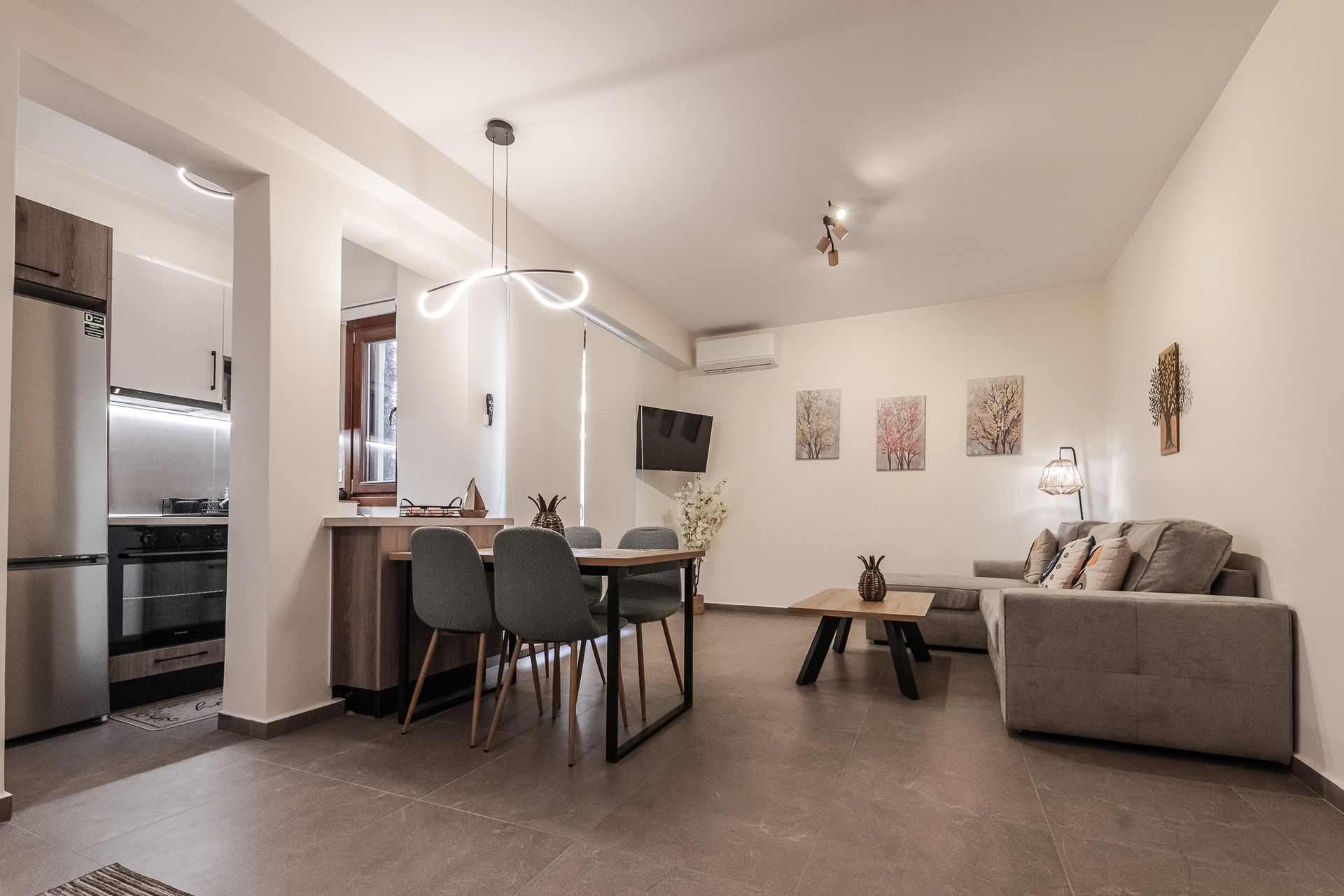 Open-plan living room with dining table, gray sofa, wall art, and kitchen pass-through opening.