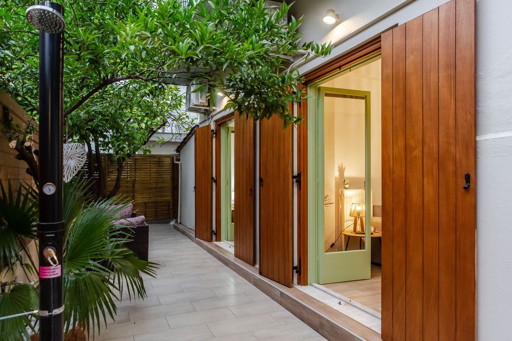Modern patio walkway with wooden doors, potted greenery, and warm interior light