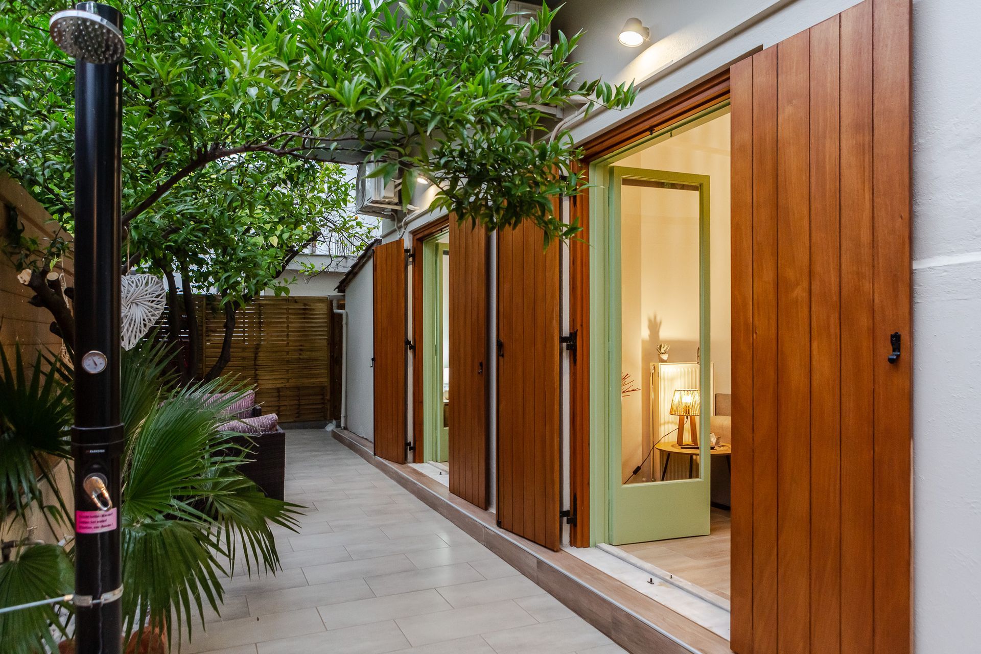 Modern patio walkway with wooden doors, potted greenery, and warm interior light