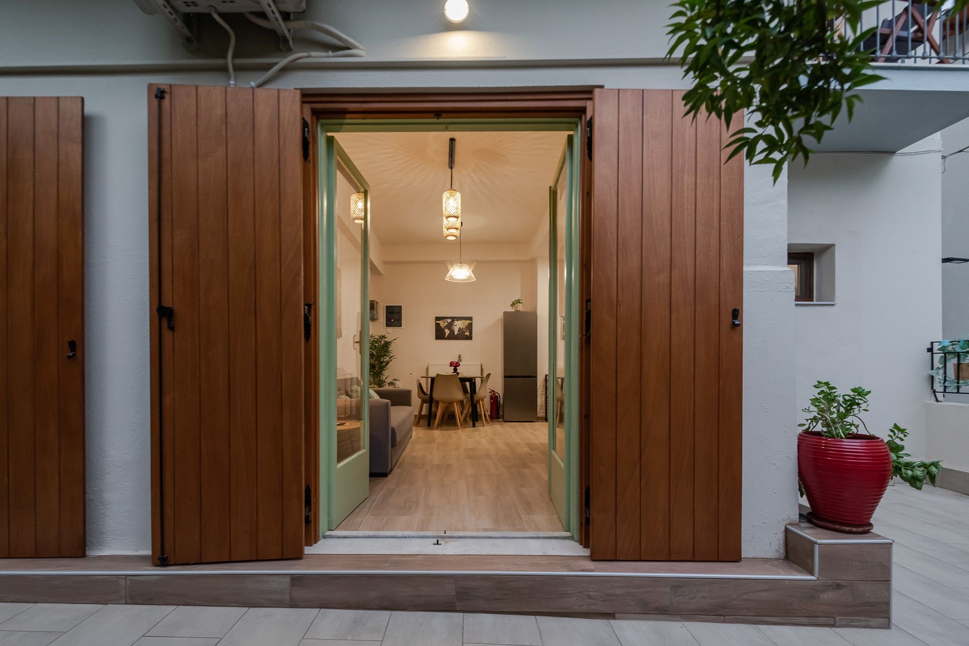 Open wooden doorway to a warmly lit interior, with potted plants and a red planter outside.