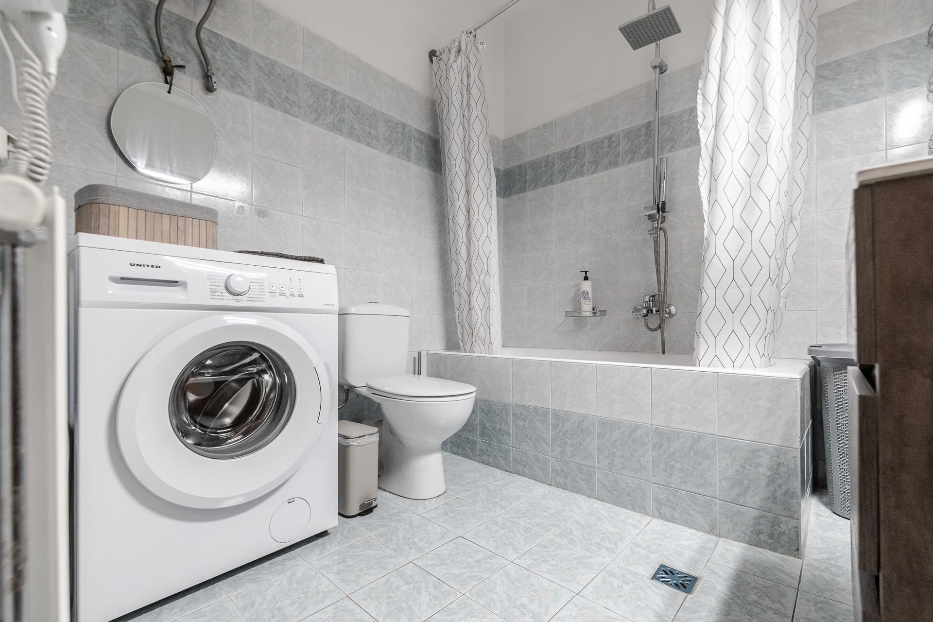 Modern white bathroom with bathtub, toilet, washing machine, and light gray tile accents