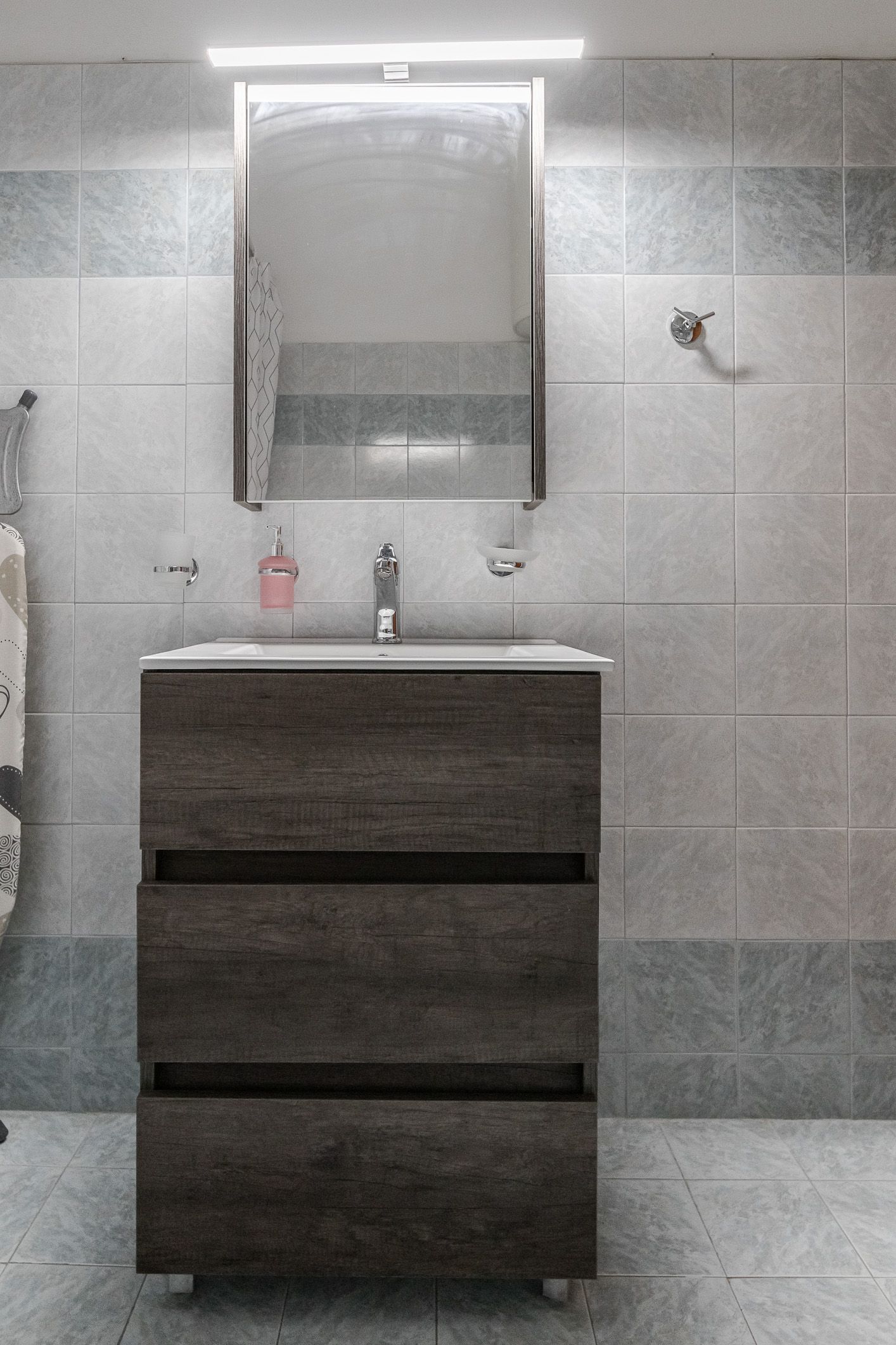 Modern bathroom vanity with mirror, sink, and wall-mounted light in gray-tiled room