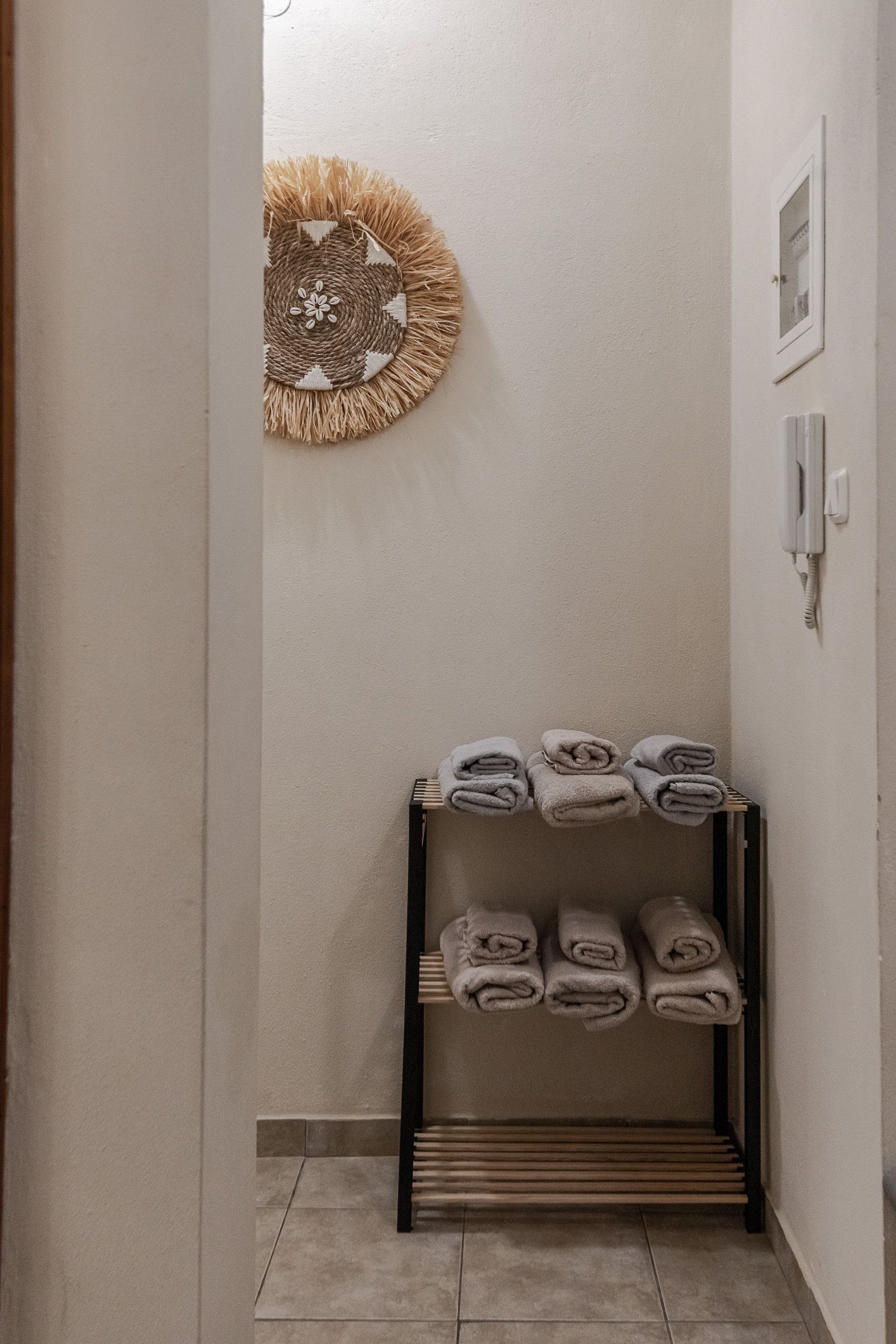 Narrow hallway with woven wall decor and a small shoe rack holding folded towels and slippers