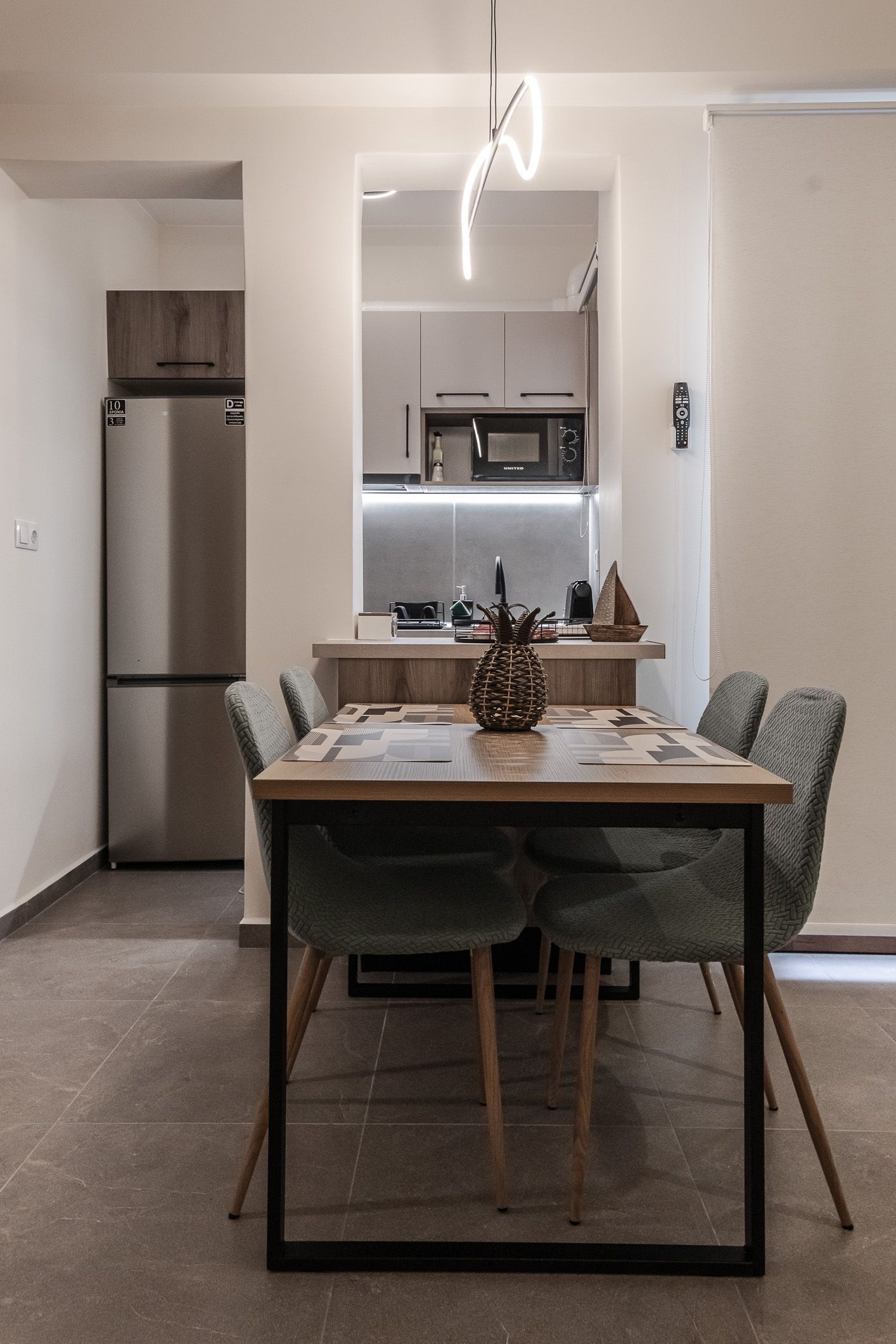 Small dining table with chairs in a modern apartment kitchen area, with a refrigerator and bar stool in the background