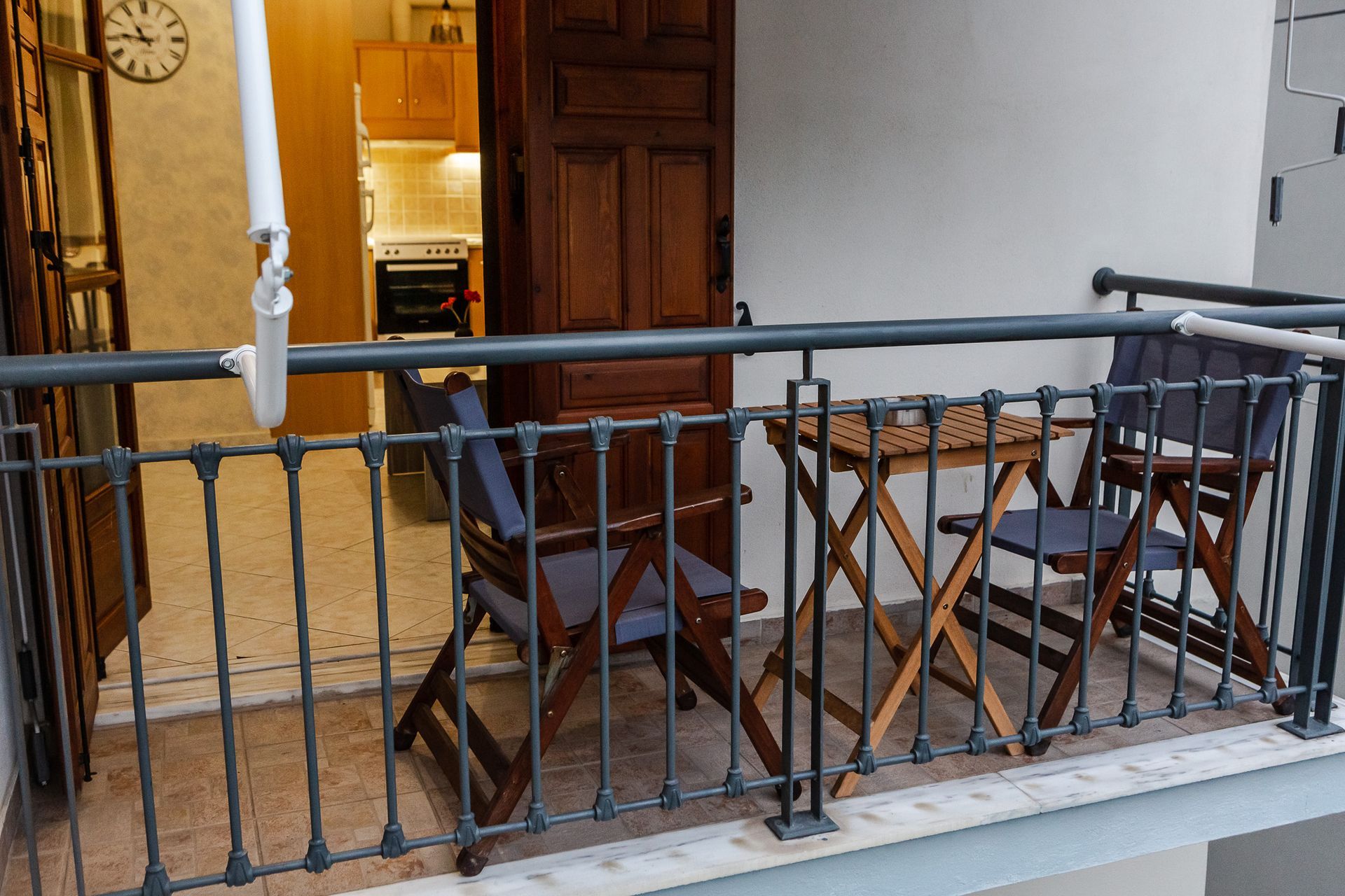 Small patio with two wooden chairs and a table behind a black metal railing, beside a doorway