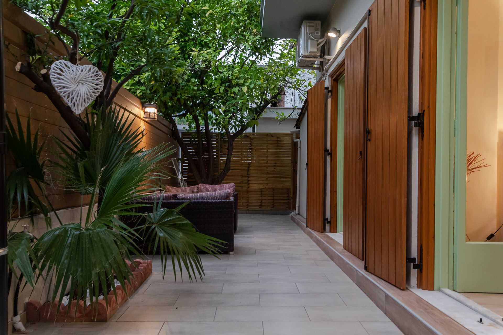 Modern patio with wooden sliding doors, tiled floor, and lush tropical plants along a narrow walkway