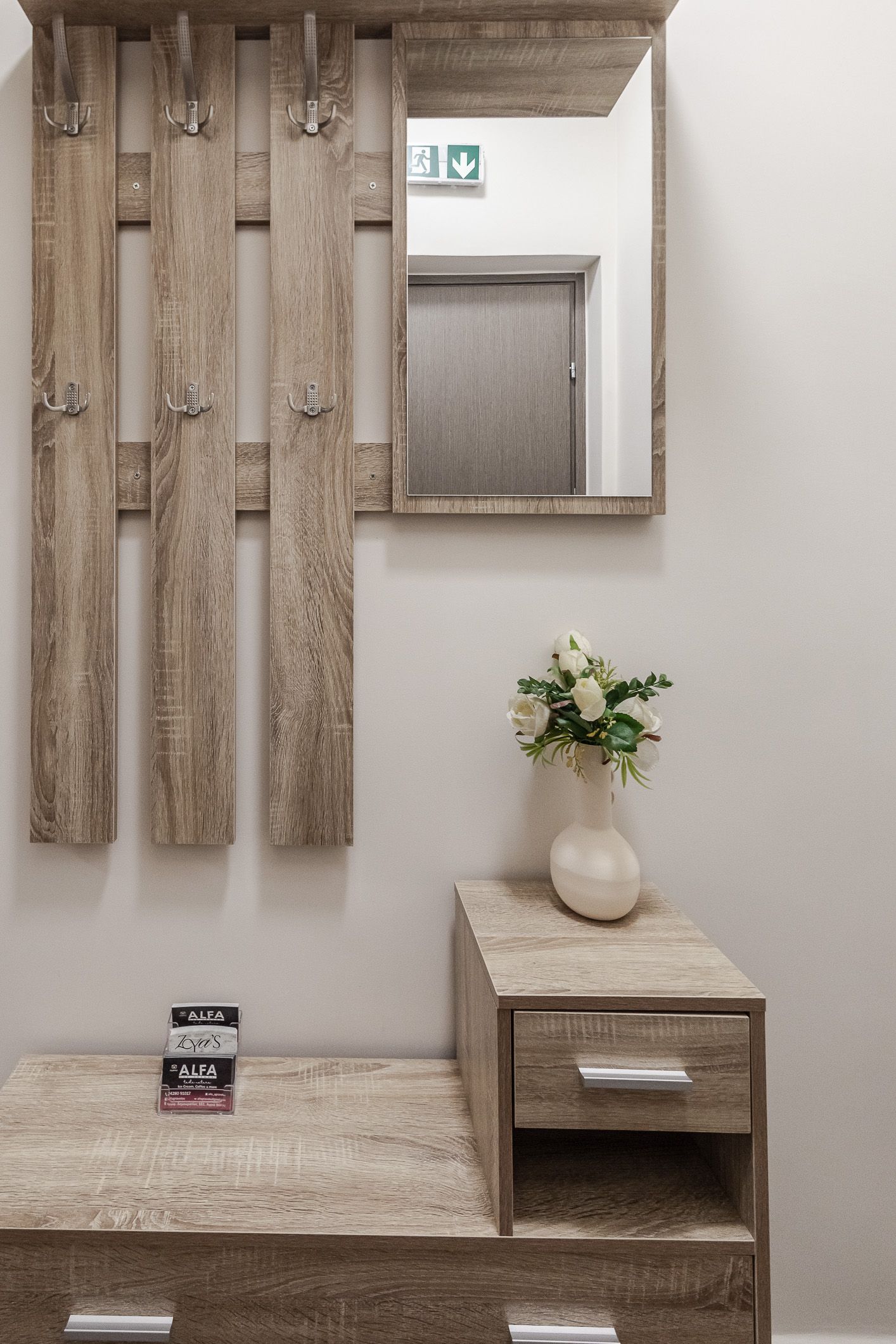 Small modern entryway with wall mirror, flowers on a side table, and a bench beneath wooden wall slats.
