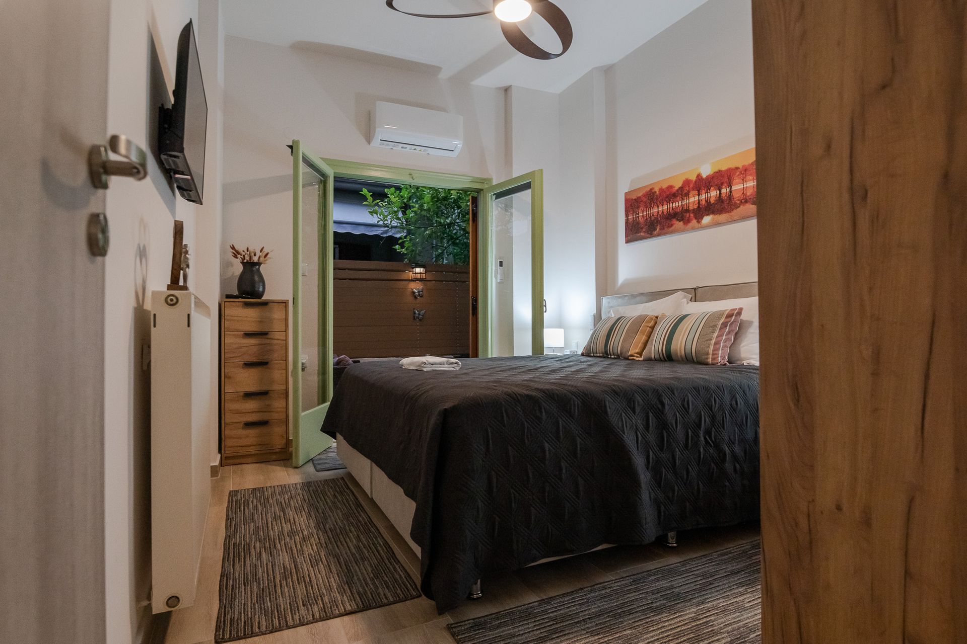 Cozy bedroom with a bed, open green balcony doors, wood furniture, and a ceiling fan