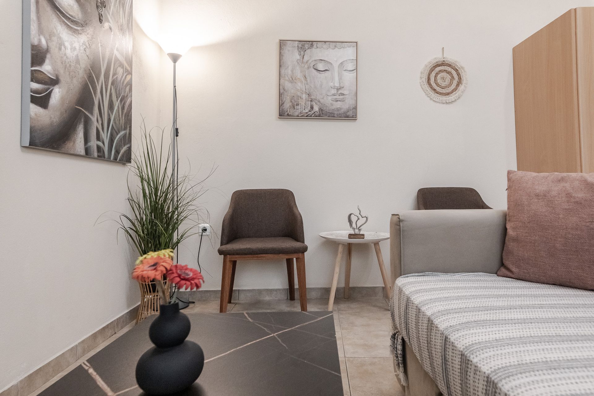 Cozy modern bedroom with gray bed, two chairs, floor lamp, artwork, and small vase of flowers