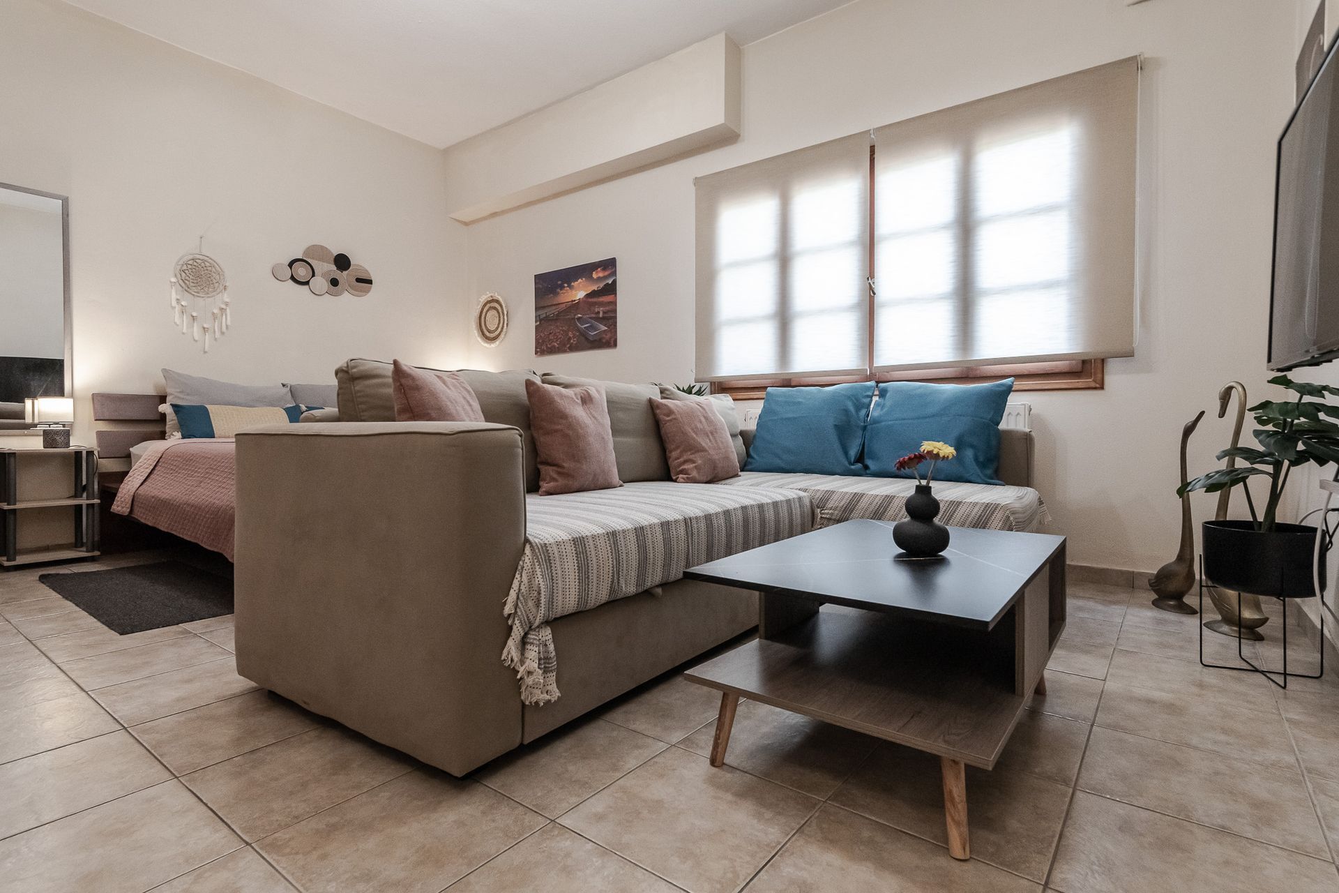 Modern living room with beige sofa, coffee table, tiled floor, and sunlight through a window