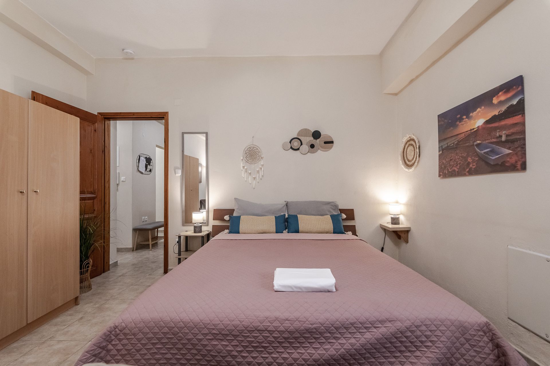 Bright bedroom with a neatly made bed, wardrobe, nightstands, and wall art.