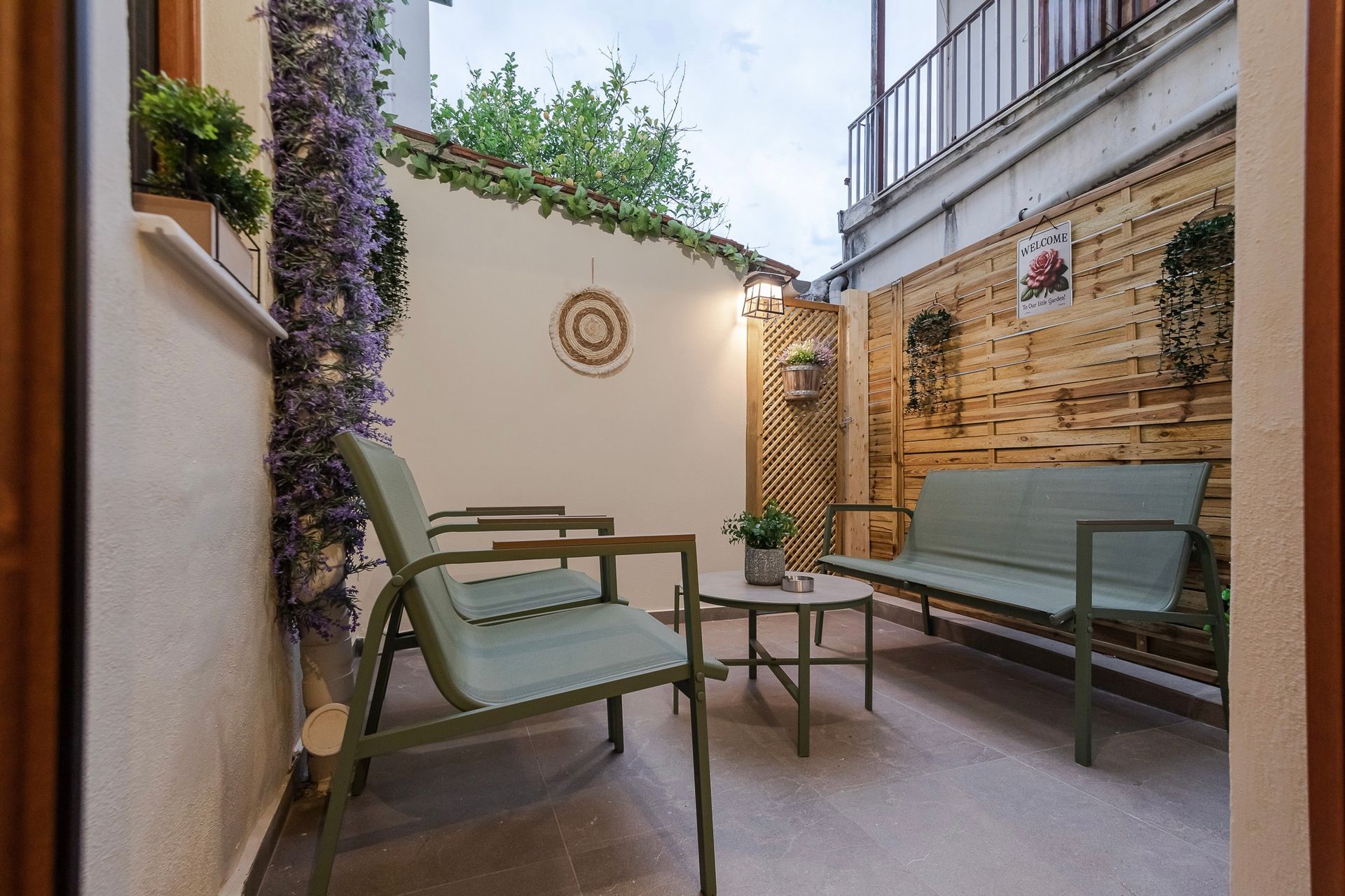 Small courtyard patio with green chairs, a bench, and a glass table against brick and stucco walls