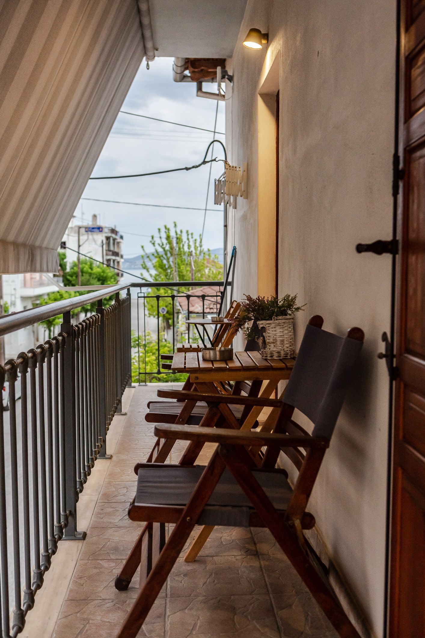Narrow apartment balcony with wooden chairs, potted plants, and railings overlooking the street.