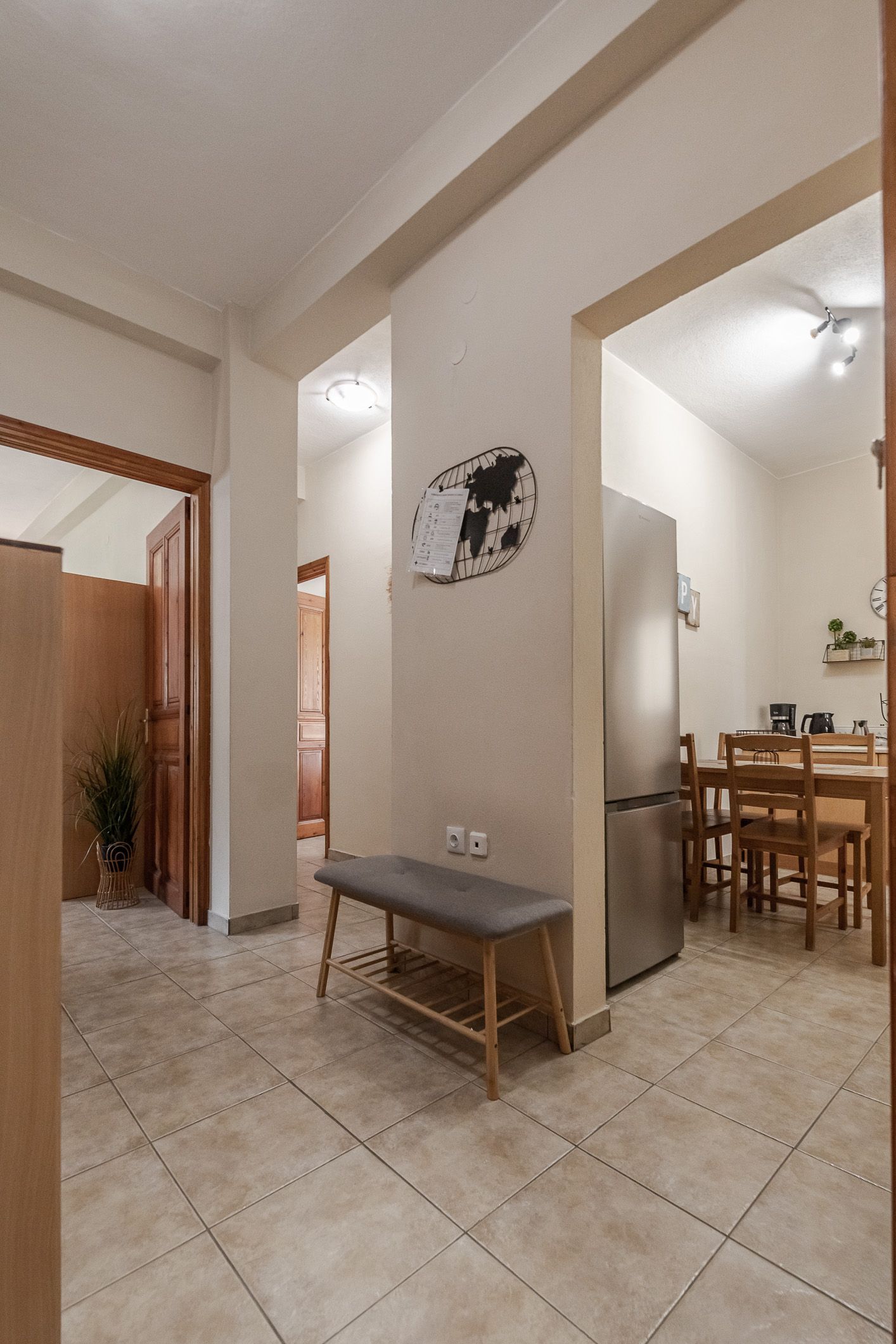 Bright tiled hallway with open archways, bench, and a dining area visible in the background