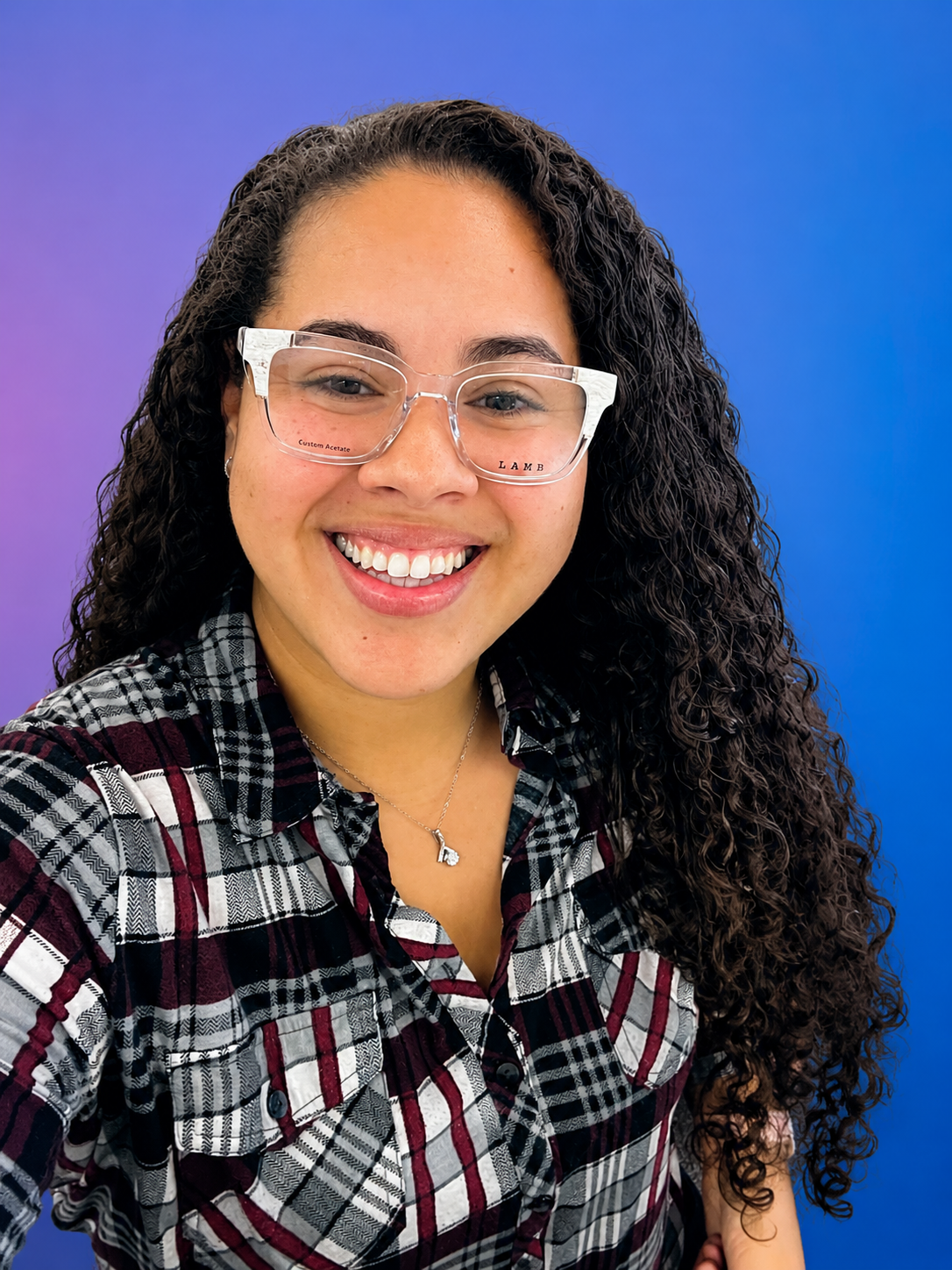 Smiling person in glasses and plaid shirt against a purple gradient background