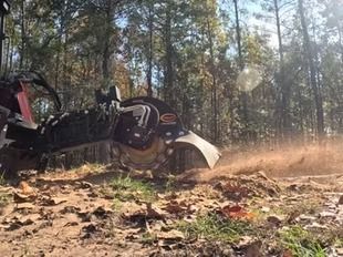 Tractor with rotary mower kicking up dust in a wooded field