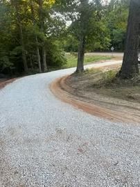Curving gravel road through wooded area with trees and dirt shoulder