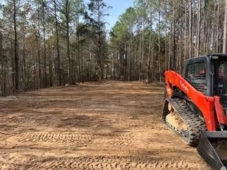 Orange excavator on a dirt path in a wooded clearing
