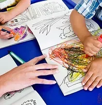 A group of children are sitting at a table drawing in coloring books.