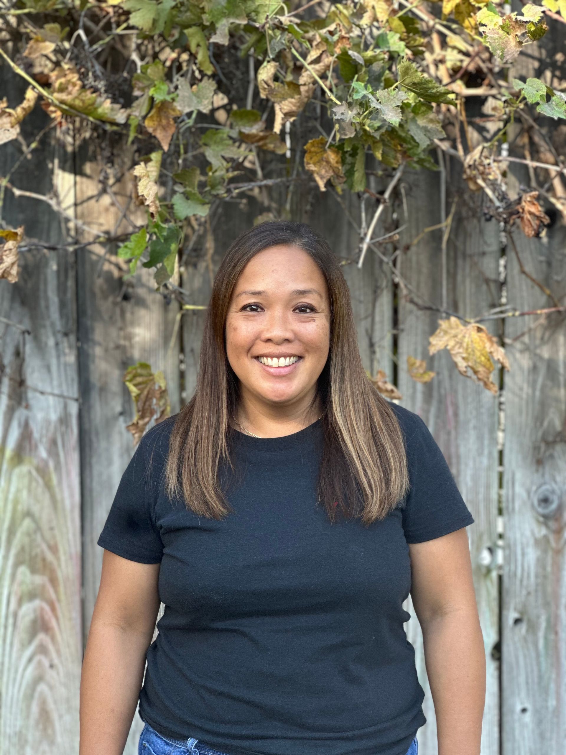 A woman in a black shirt is standing in front of a wooden fence.