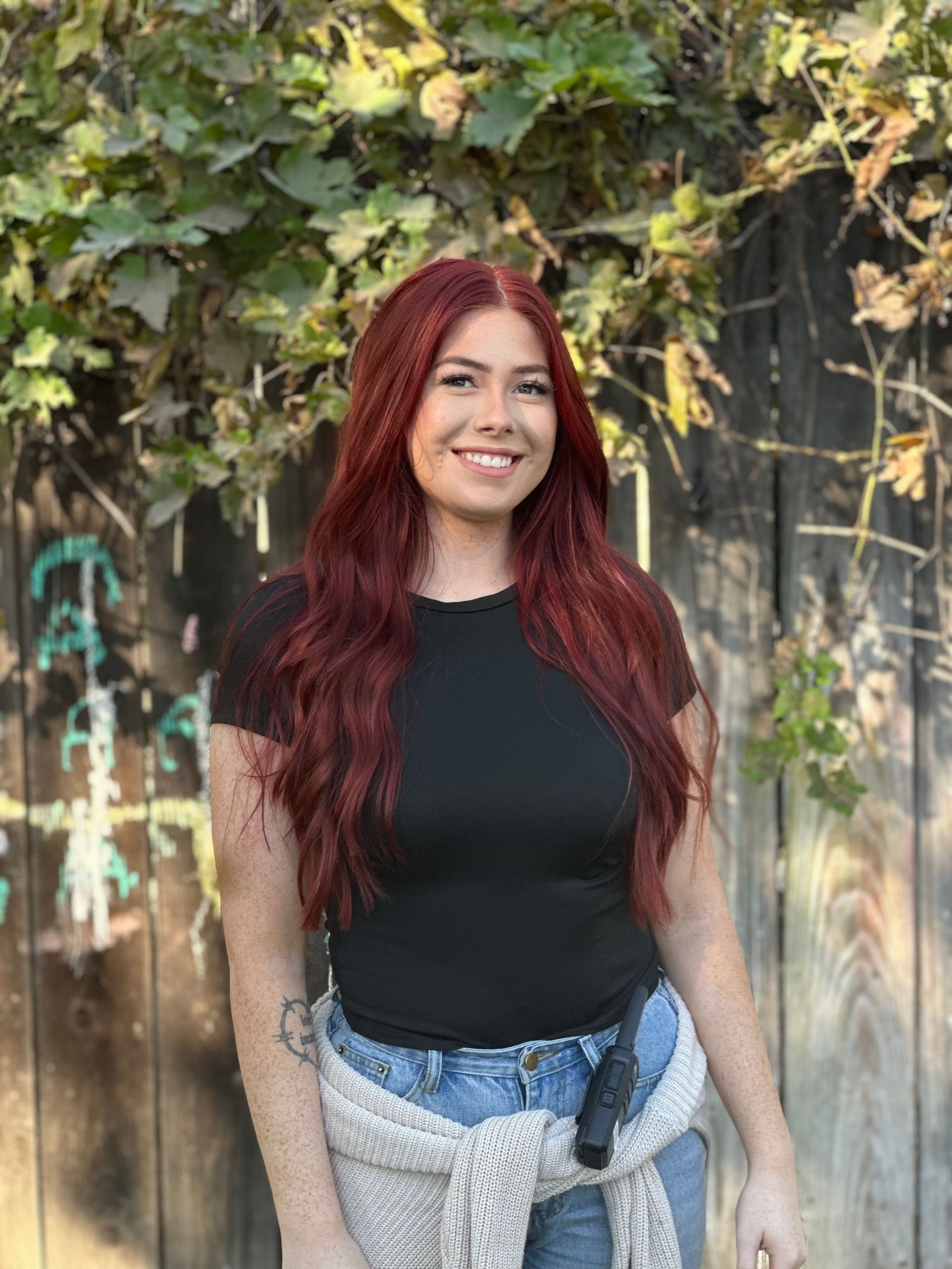 A woman with red hair is standing in front of a wooden fence.
