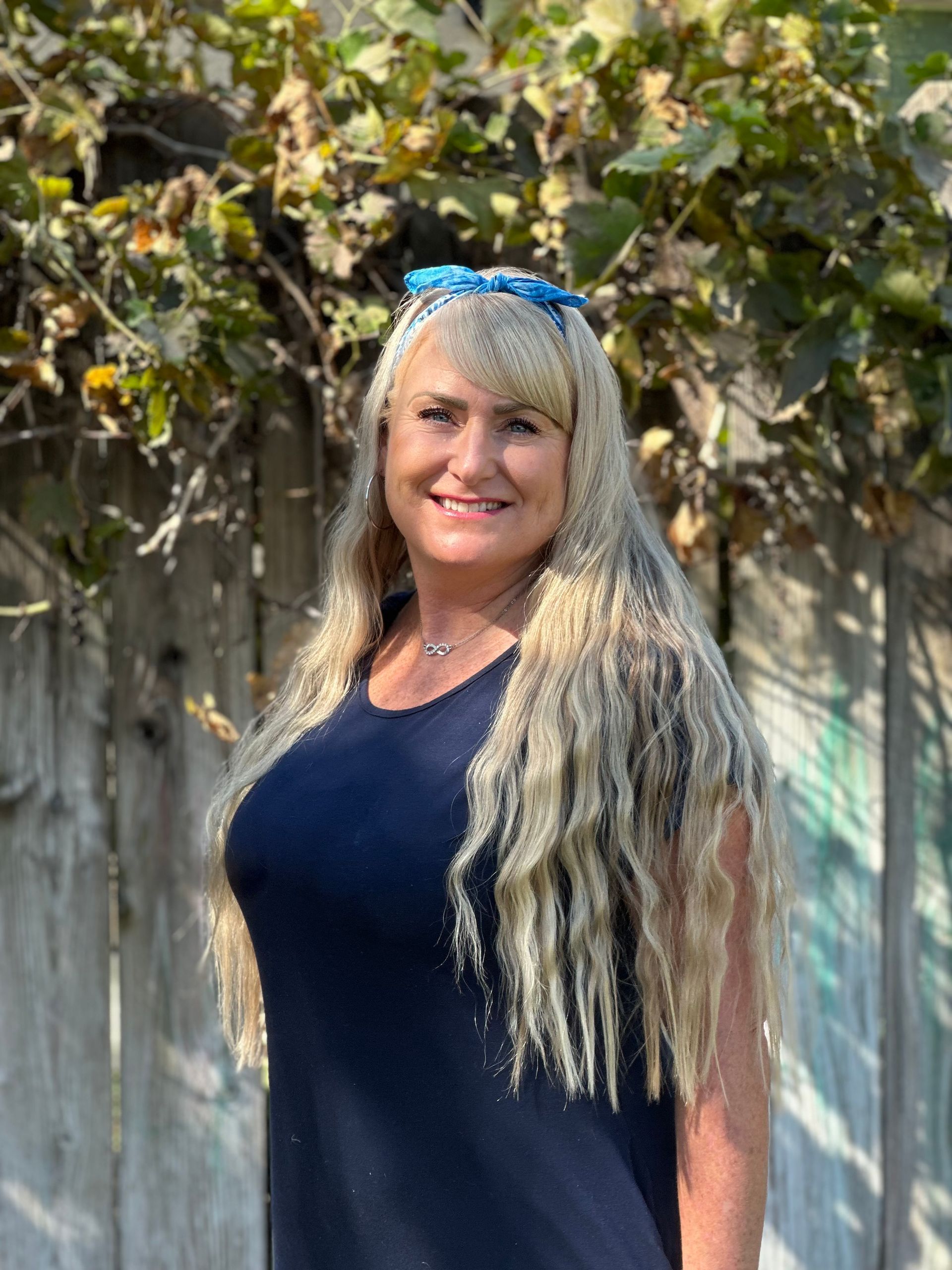 A woman in a blue dress is standing in front of a wooden fence.