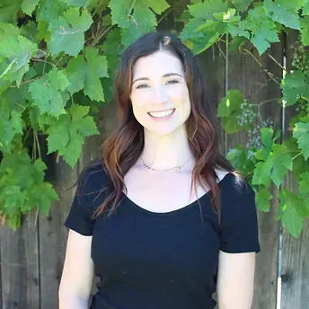 A woman in a black shirt is smiling in front of a wooden fence.