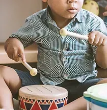A young boy is sitting on the floor playing a drum.
