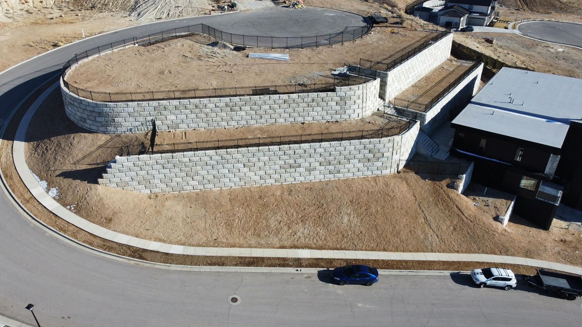 Aerial view of a terraced stone landscape beside a curved road with a few parked cars and a building
