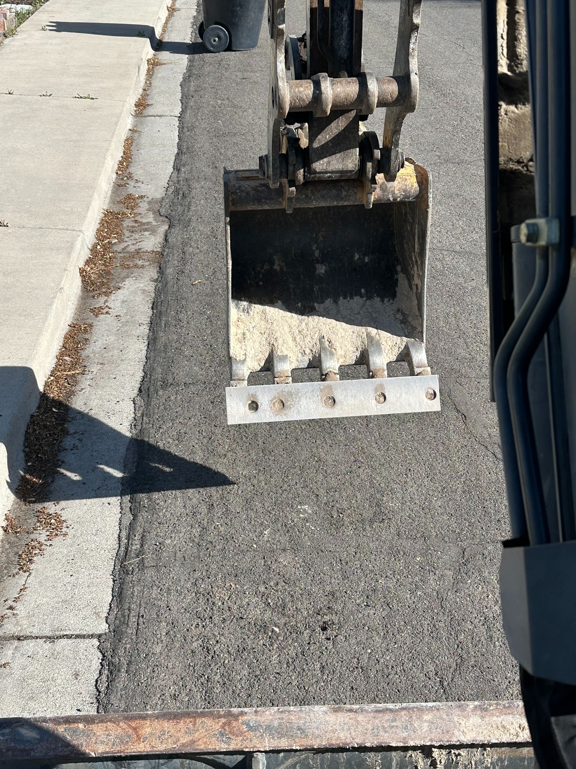 Construction bucket full of gravel on a paved curbside strip next to a street