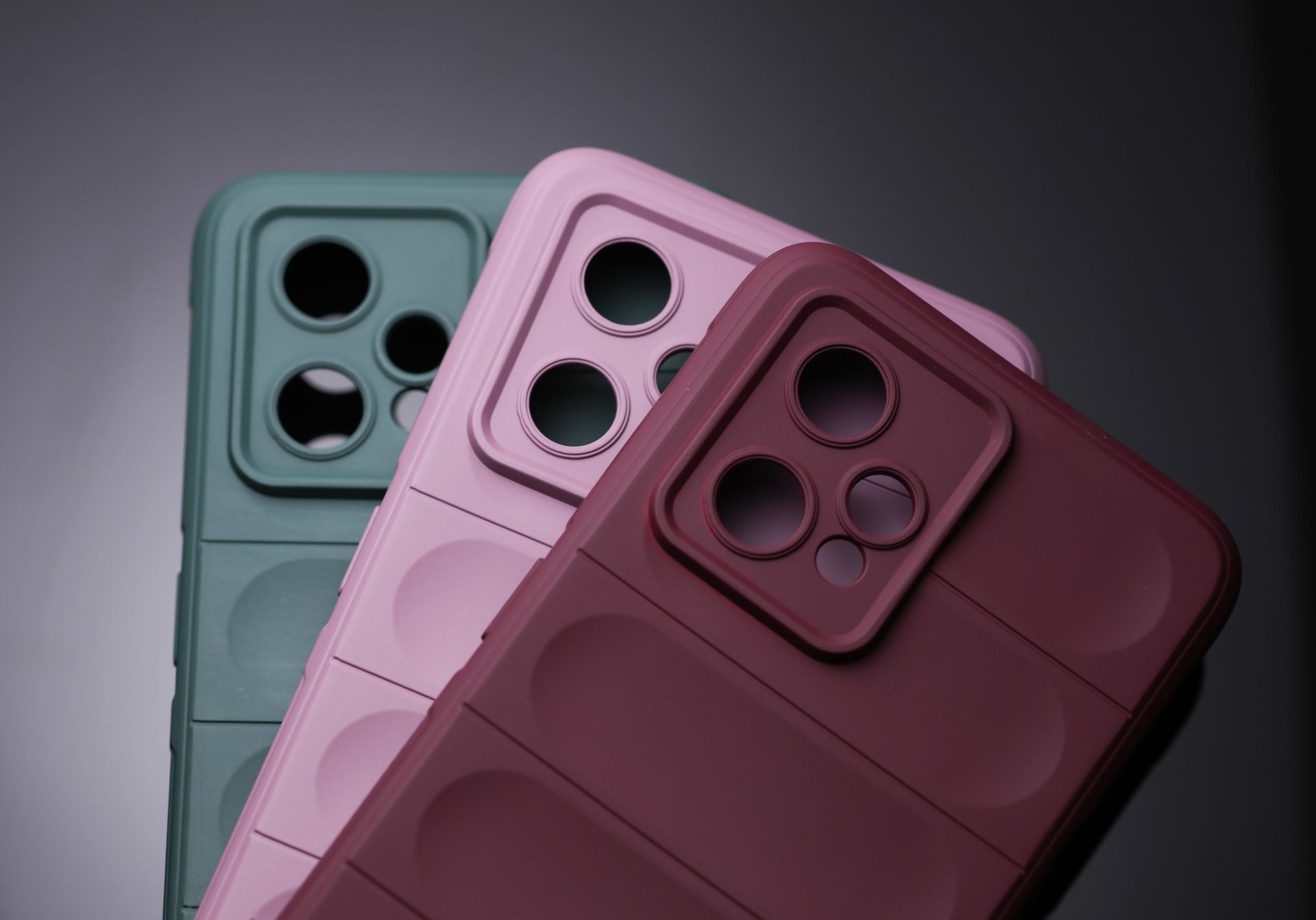 Tres coloridas fundas para smartphones con grandes recortes para la cámara sobre un fondo oscuro.