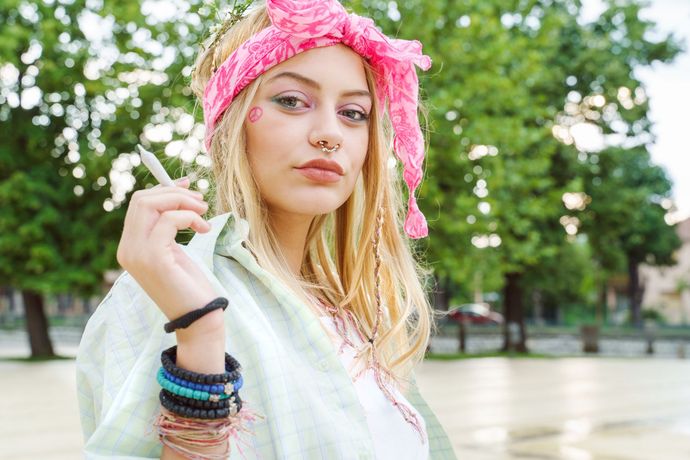 Woman wearing a pink floral headscarf and bracelets, standing outdoors in a park.