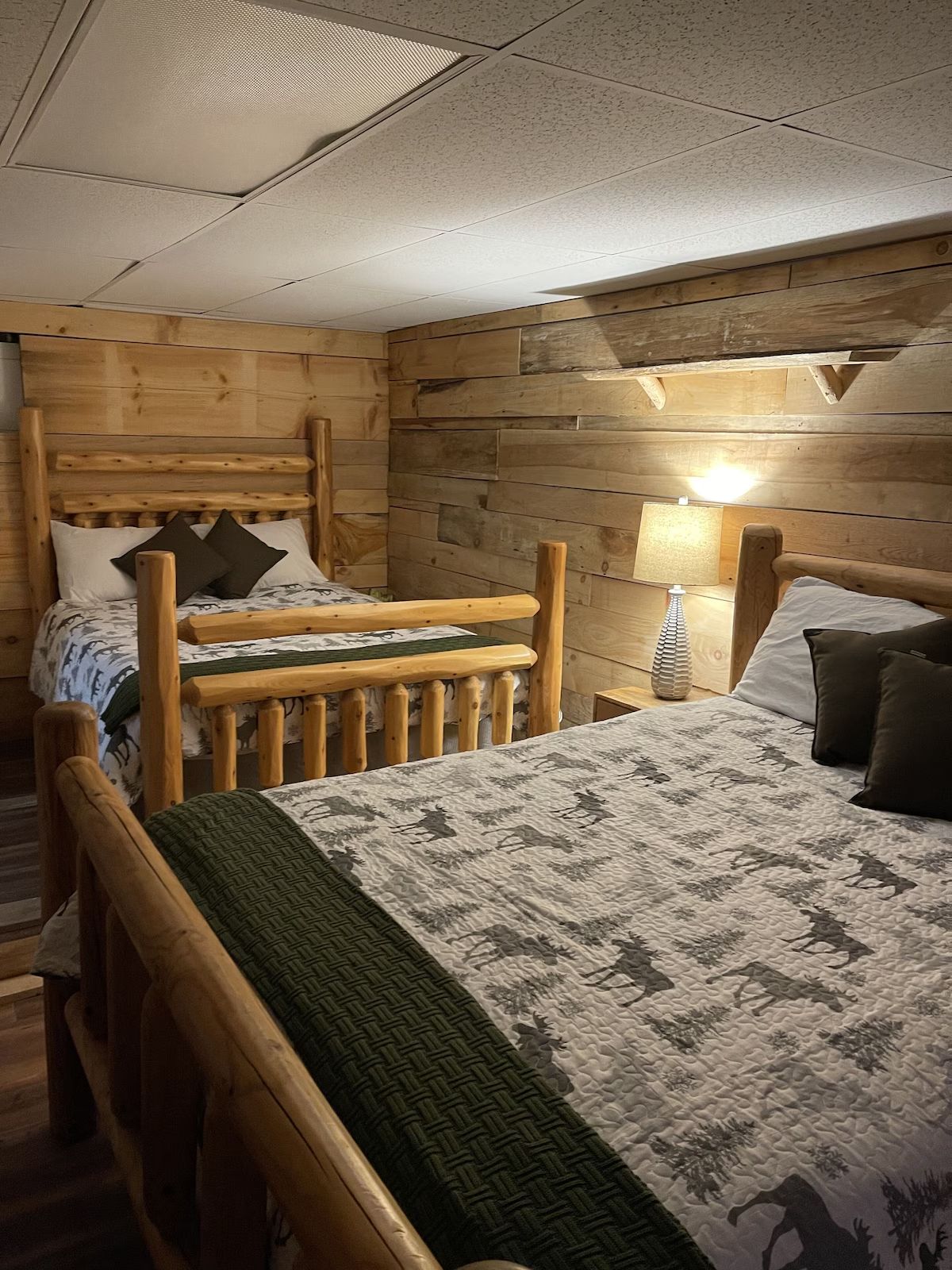Two log-framed beds in a rustic-style bedroom with wood-paneled walls and dim lighting.