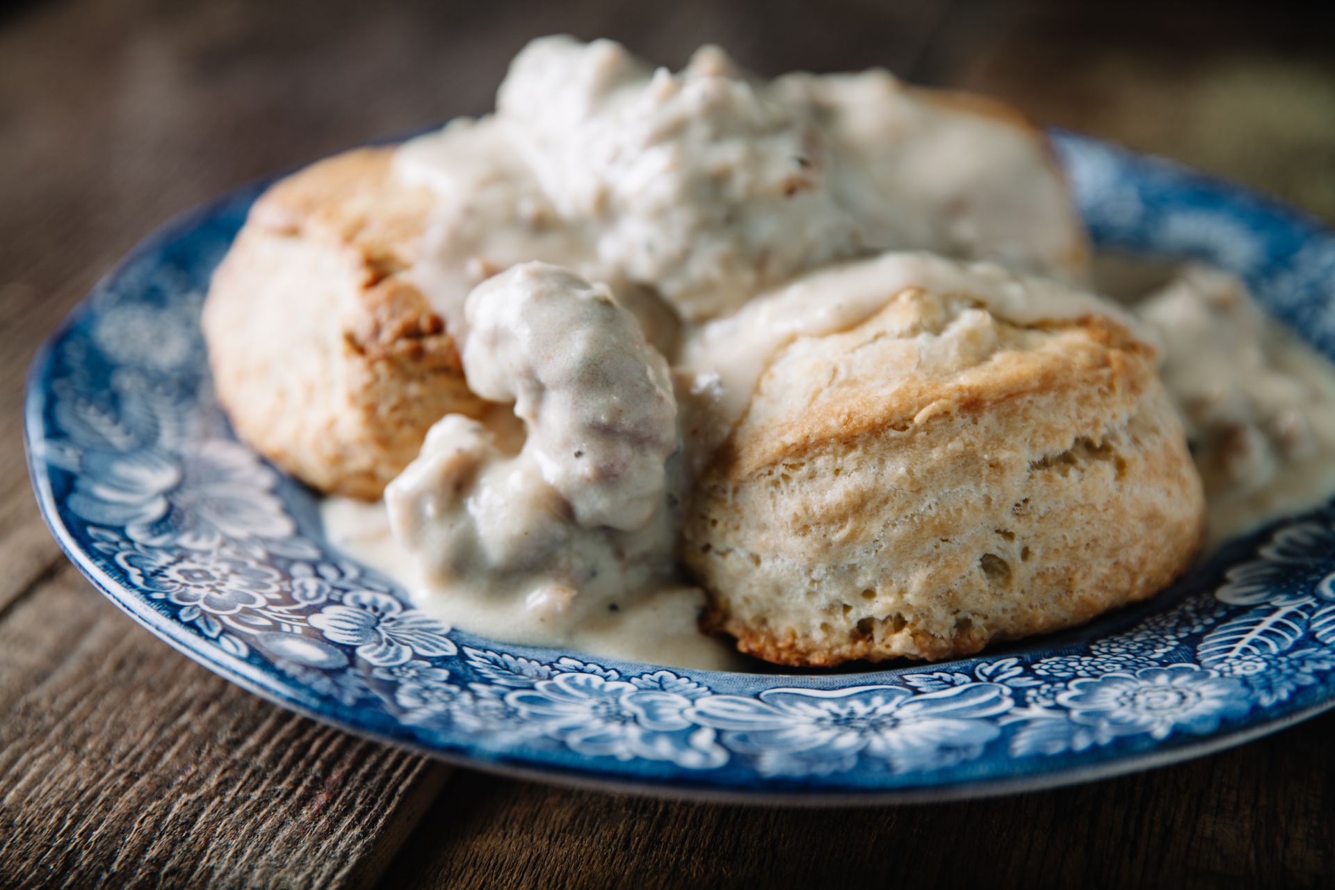 Biscuits and gravy on a blue patterned plate on a wooden table.