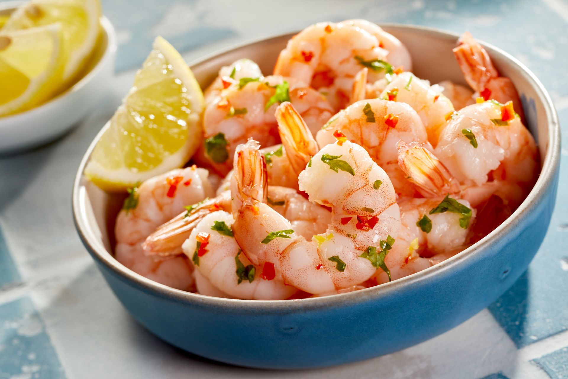 Bowl of cooked shrimp with lemon wedges, garnished with herbs and chili flakes.