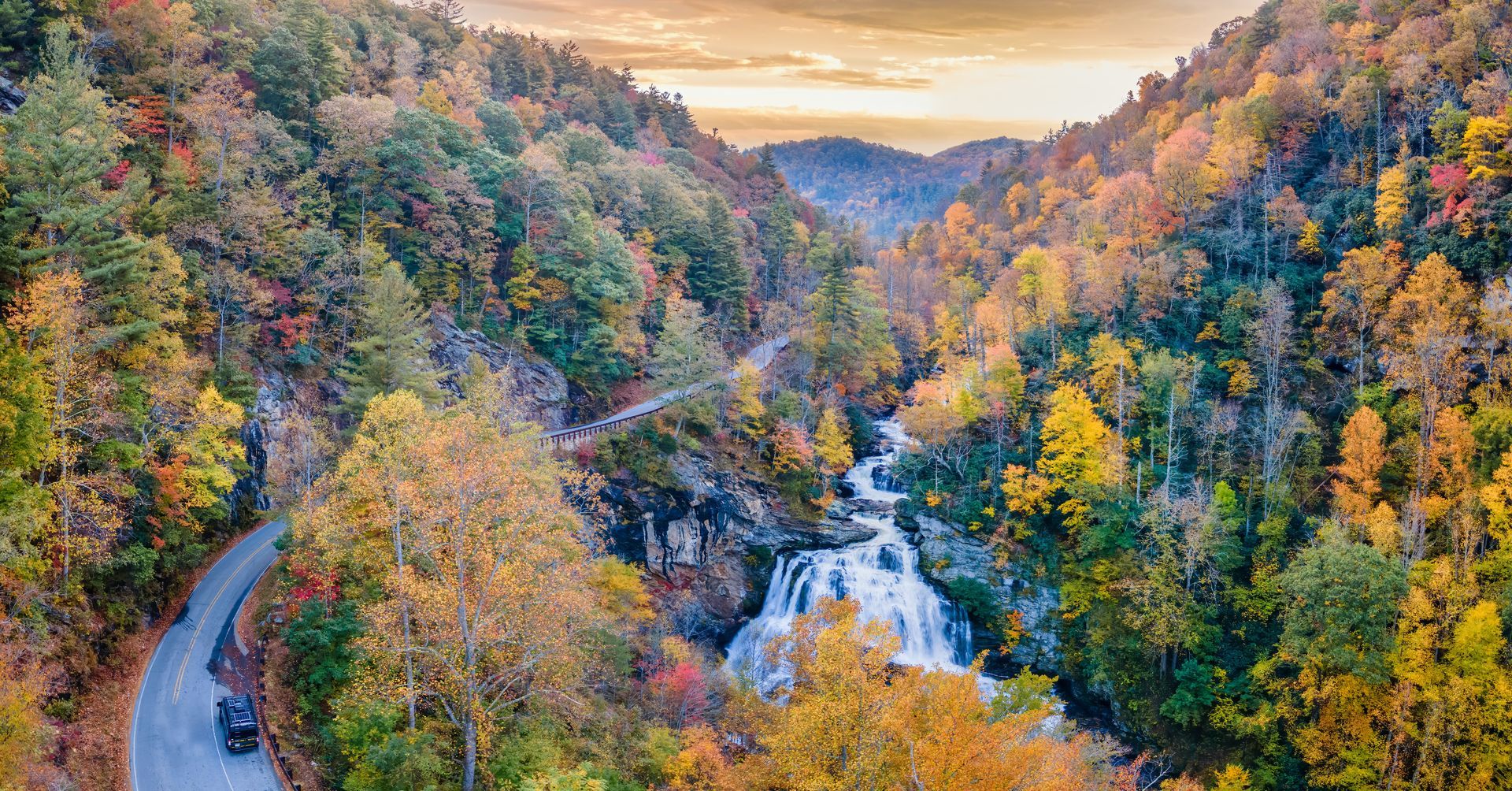 Autumnal mountain scene with winding road, waterfall, and colorful trees.