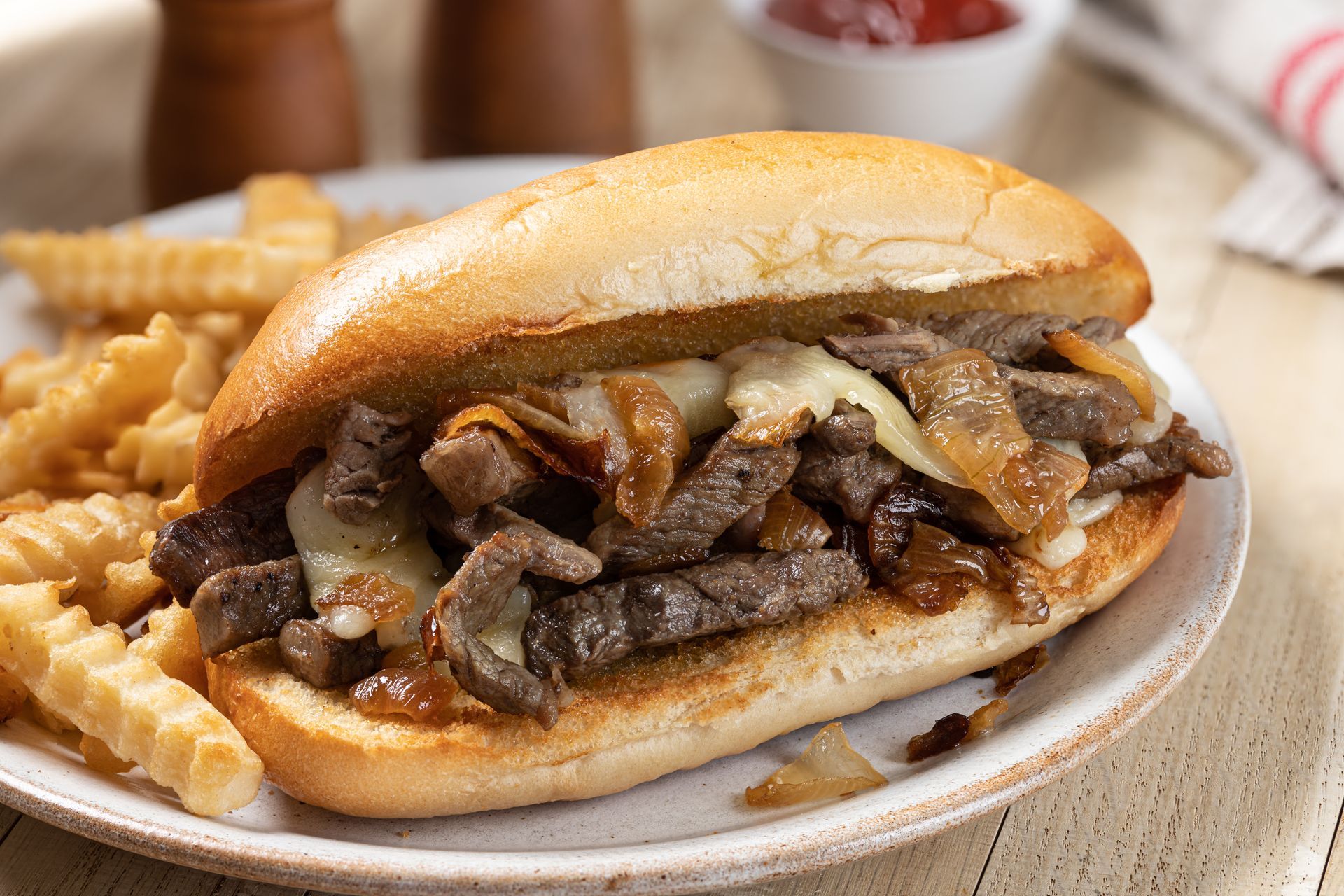 Cheesesteak sandwich with grilled onions and fries on a plate.