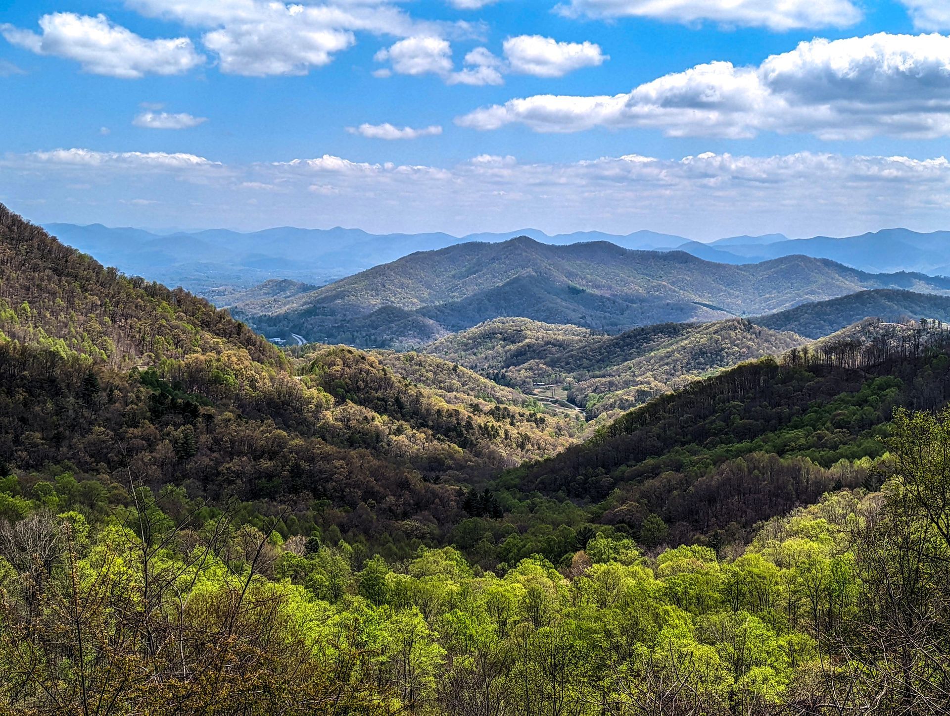 Rolling mountain range under a blue sky with puffy white clouds, green and brown trees.