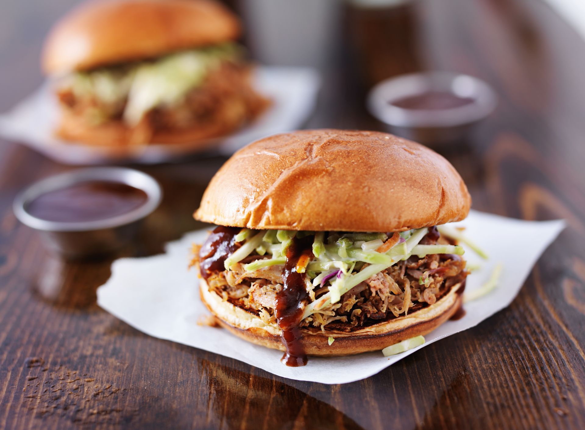 Pulled pork sandwich with coleslaw and BBQ sauce on wooden table.