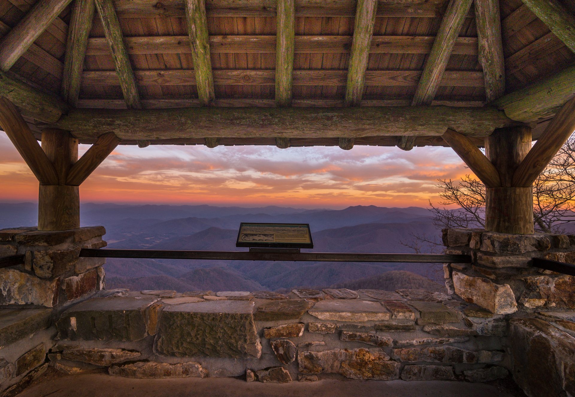 Gazebo frames a sunset over distant mountains. Warm orange and purple hues fill the sky.