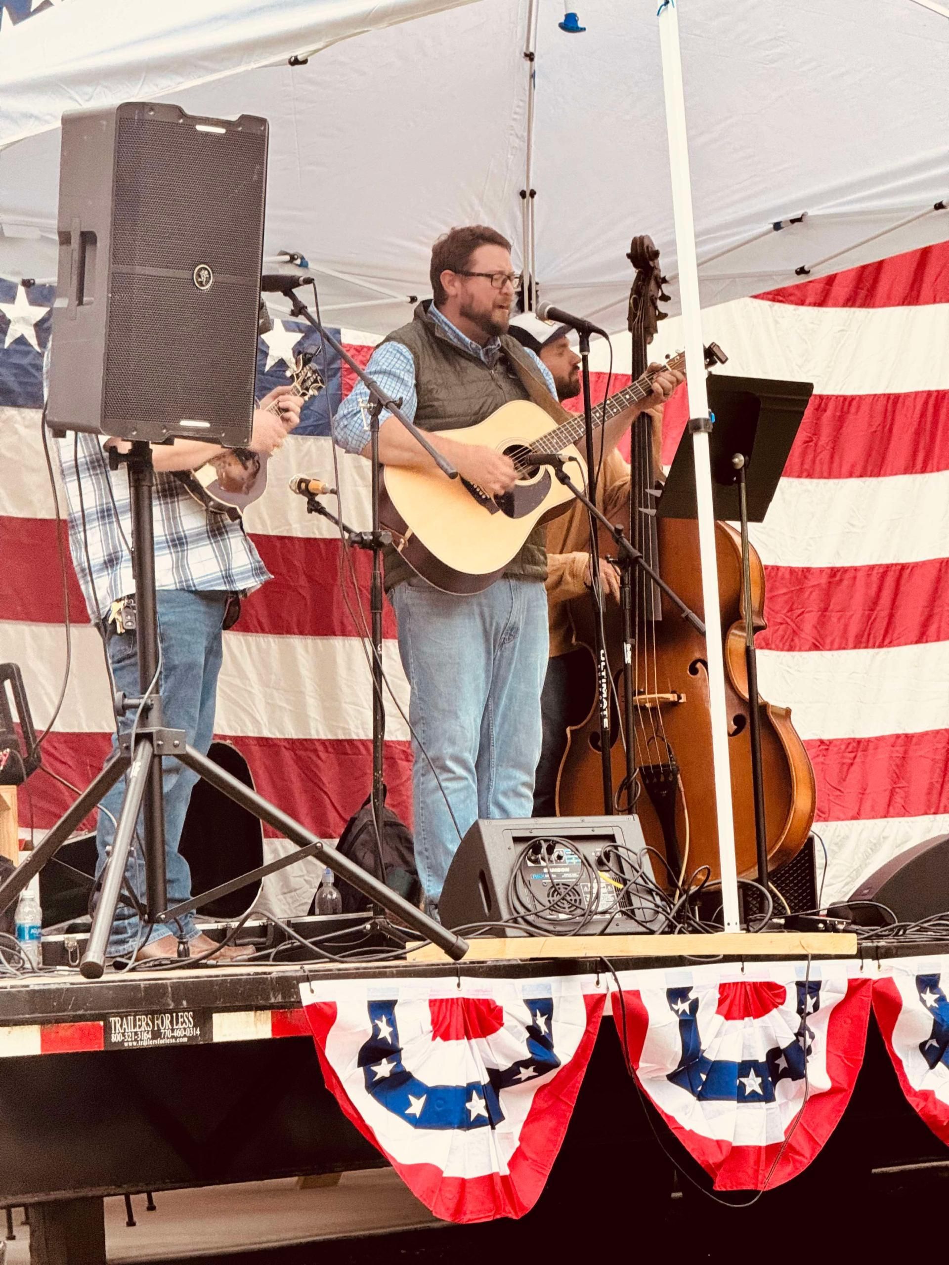 Band playing on a stage with an American flag backdrop. A man sings and plays guitar.