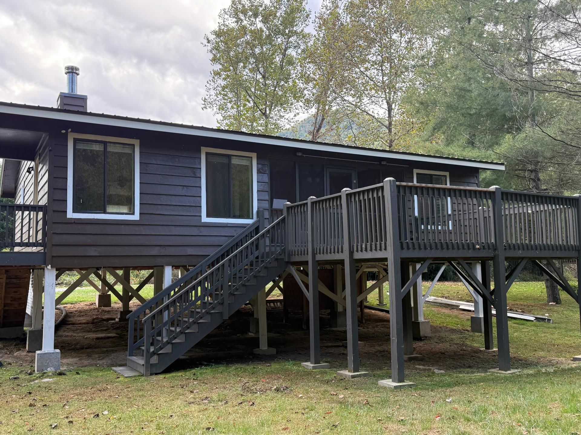 Dark cabin with deck and stairs, elevated on posts, set in grassy yard.