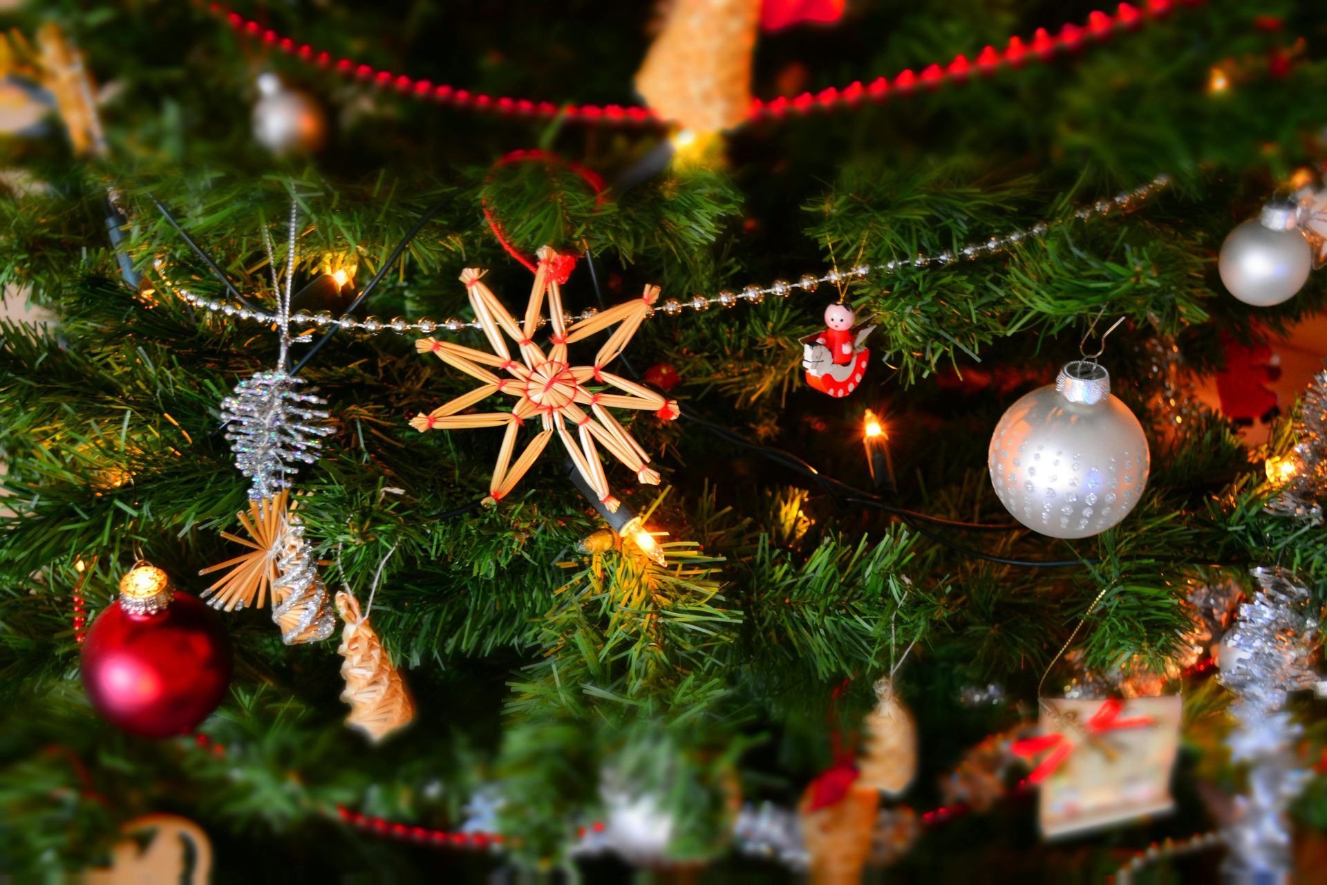 Christmas tree decorated with ornaments, including red and silver baubles and a straw star.