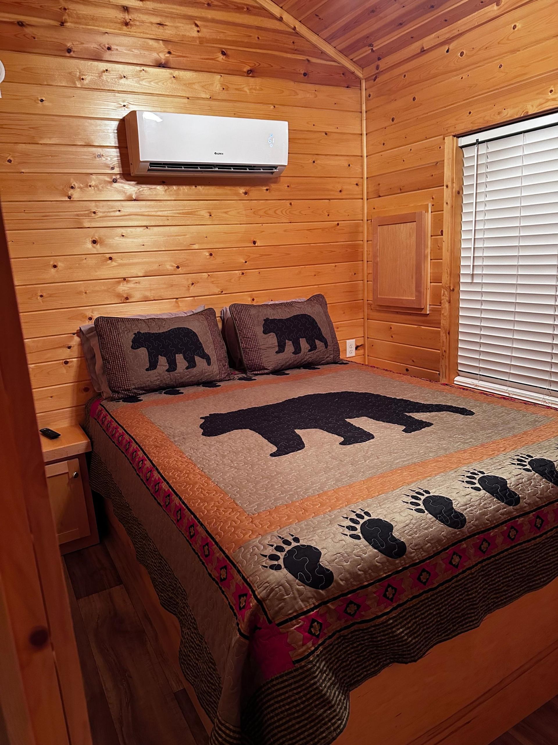 Bedroom with a bear-themed quilt and pillows, wooden walls, and a window with blinds.