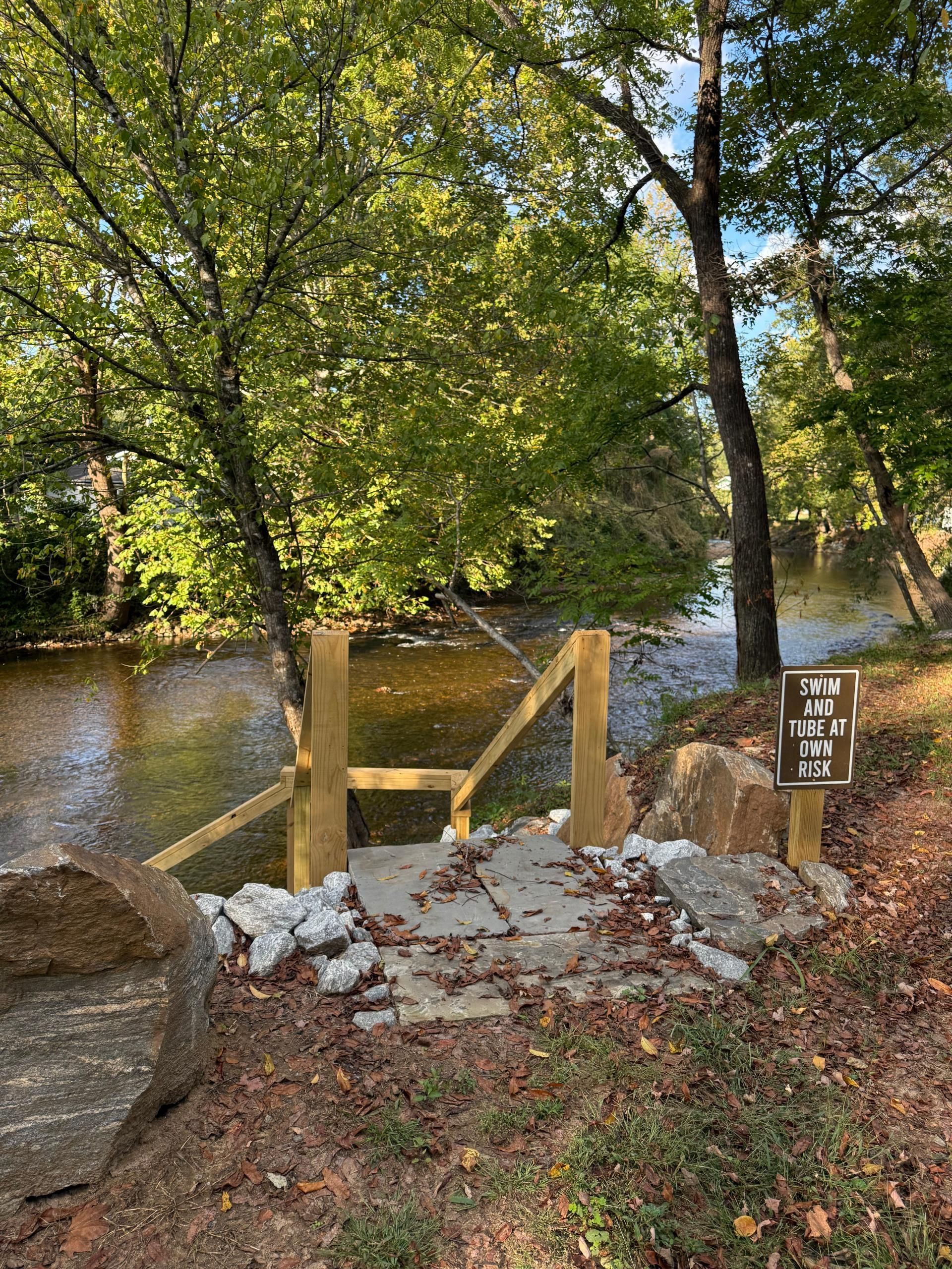 Wooden bridge over a river, with a sign, trees, and large rocks.