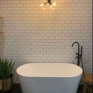 Oval bathtub in a bathroom with white brick wall, black faucet, and plant.