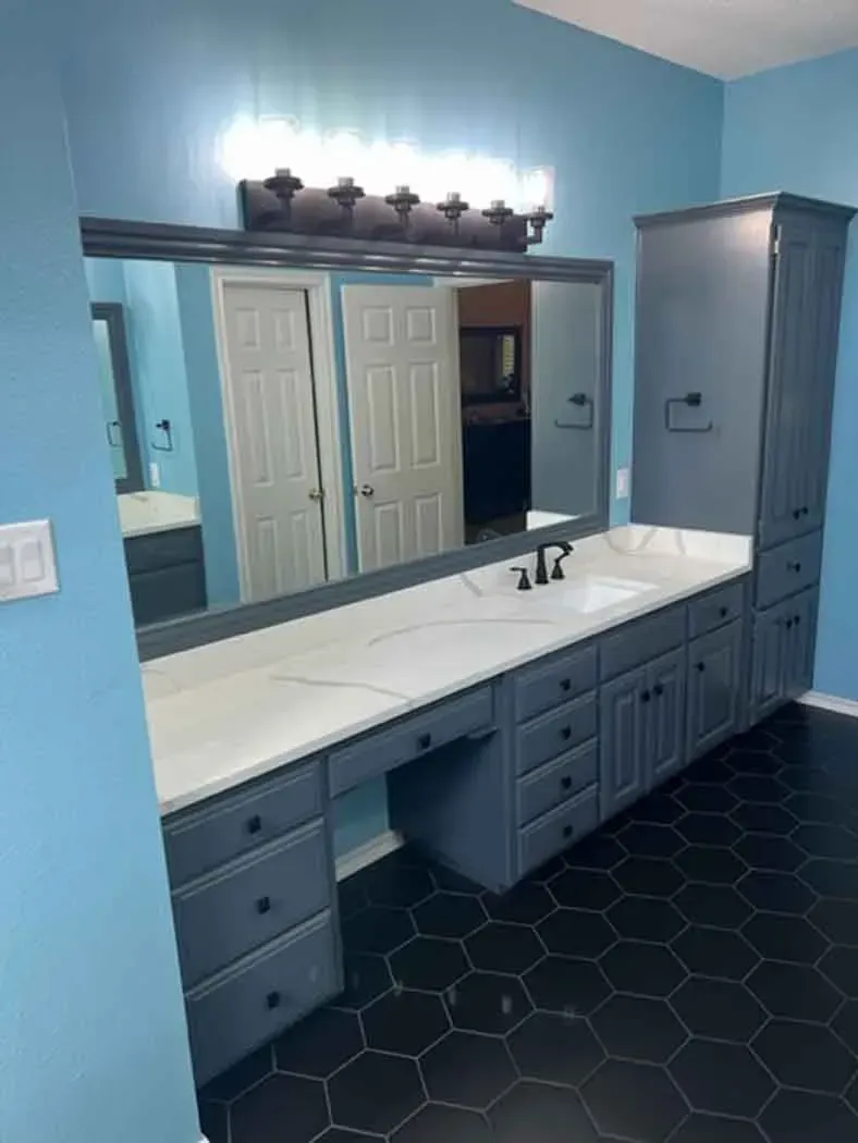 Blue bathroom with a long countertop, vanity, and a tall storage cabinet. Black hexagonal floor tiles.