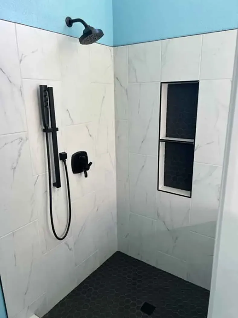 Bathroom with white marble tiles, black fixtures, shower head, and recessed shelf. Black hexagonal tile floor and blue walls.