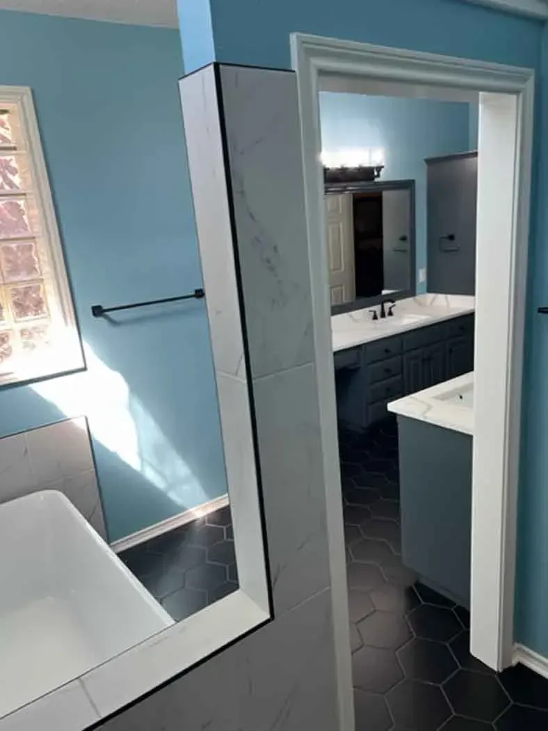 Bathroom interior with blue walls, black hexagon floor tiles, and a white soaking tub.